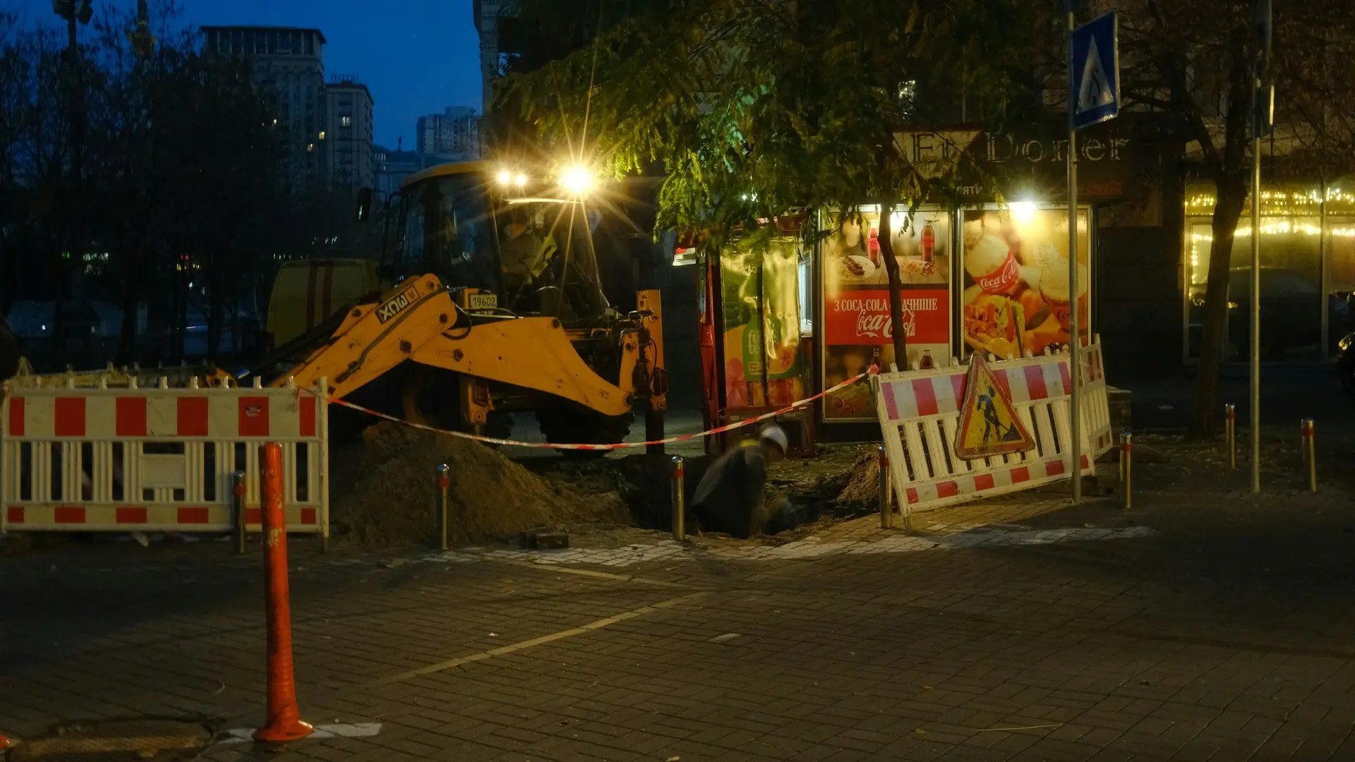 A backhoe at a barricaded nighttime street excavation.